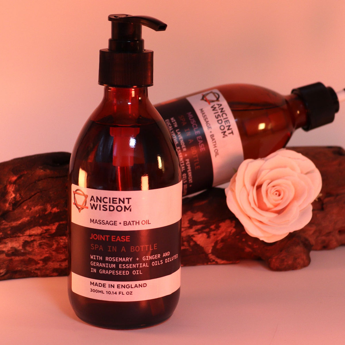 Bottle of Ancient Wisdom massage and bath oil with a pink flower on a wooden surface.