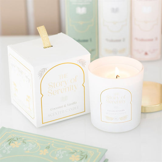 White candle with gold text 'The Story of Serenity' next to its packaging on a light surface.