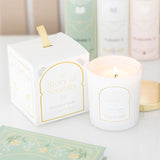 White candle with gold text 'The Story of Serenity' next to its packaging on a light surface.