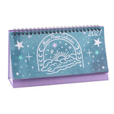 A 2027 Moon Phase Calendar desk calendar with a purple base and a light blue cover decorated with white celestial illustrations of stars, moons, and a sun rising from clouds.
