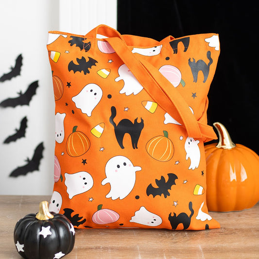 An orange tote bag with a pattern of white ghosts, black bats, and orange pumpkins on a wooden surface, with a black cat decoration and a pumpkin in the background.