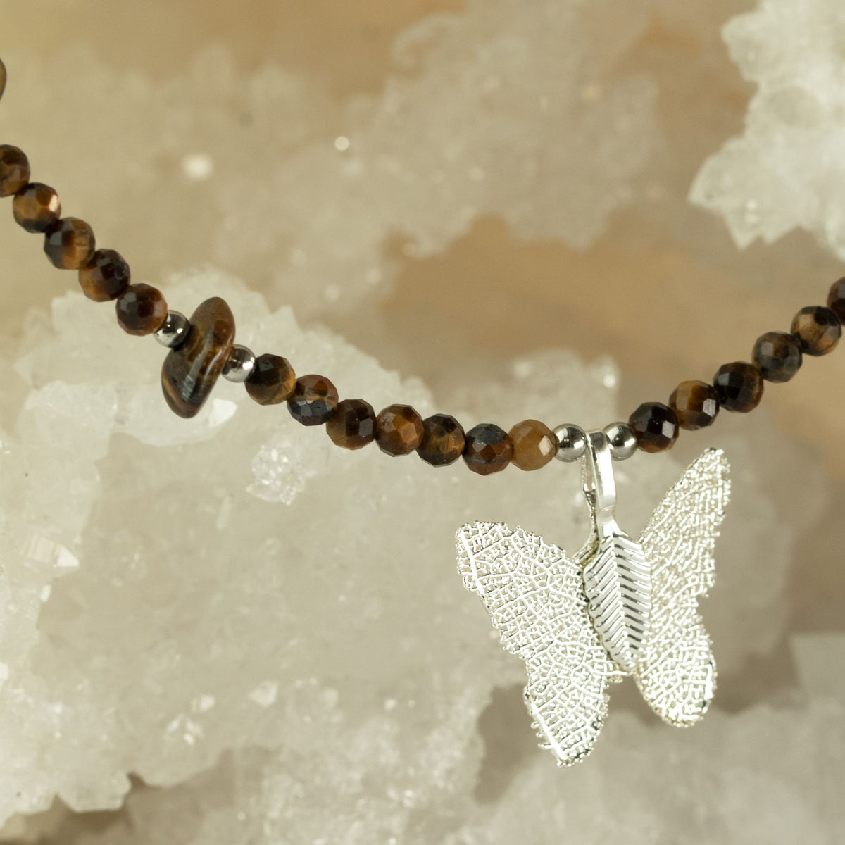 Tiger's Eye gemstone necklace with silver-plated butterfly pendant displayed on crystals
