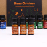 Set of Christmas-themed fragrance oil bottles with a decorative box in the background.