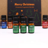 Set of Christmas-themed fragrance oil bottles with a decorative box in the background.