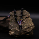 Necklace with black beads and purple accents on a dark rock background
