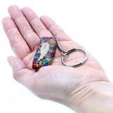 Colorful keychain with a wing design held in a hand against a white background