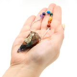 Hand holding a crystal pendulum with colorful beads on a white background