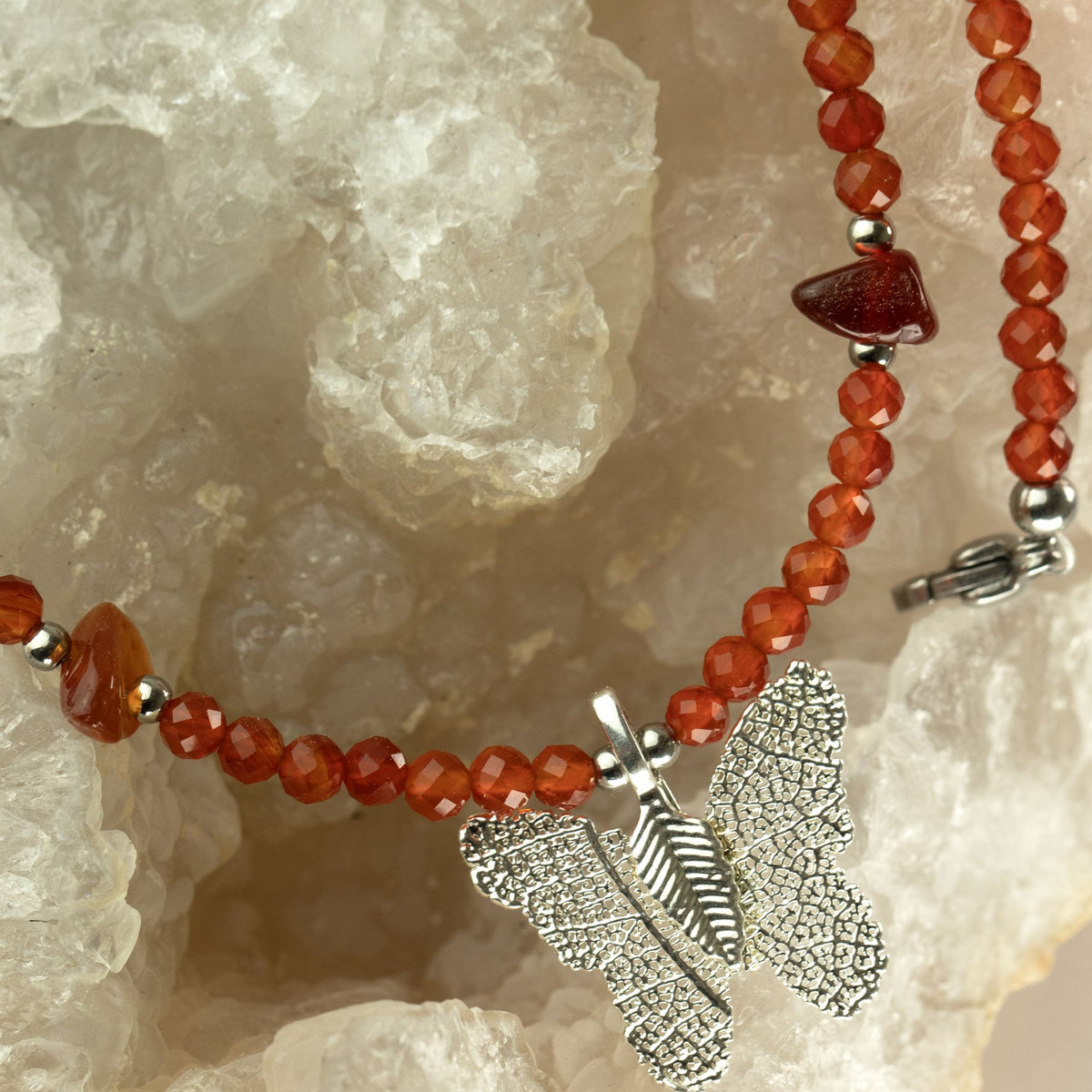 Ruby gemstone necklace with real leaf butterfly pendant displayed on crystals