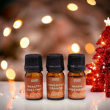 Three essential oil bottles with labels in front of a festive background with lights and a small Christmas tree.