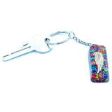 Keychain with a key, multicolored resin piece, and silver angel wing charm on a white background