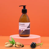 Bottle of Ancient Wisdom hand and body lotion on a pink platform with blackberries and almonds against an orange background
