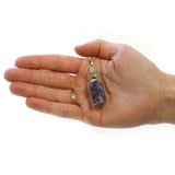 Hand holding a small glass bottle pendant with a white background