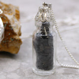 Glass bottle pendant with dark stones inside on a neutral background