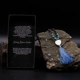 Necklace with blue tassel on a dark stone surface with descriptive text card.