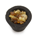 Black container with a small amount of amber-colored resin-like substance on a white background