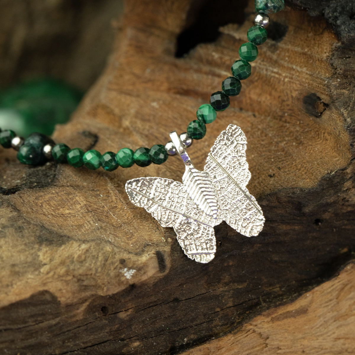 Malachite butterfly pendant necklace displayed on natural wood