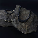 Black beaded necklace on a dark rock with a black background