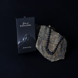 Black beaded necklace on a rock with a black box labeled 'Essence of the Numinous' on a dark background