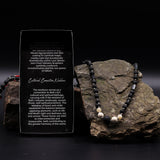 Necklace with black and white beads on a rock next to an information card