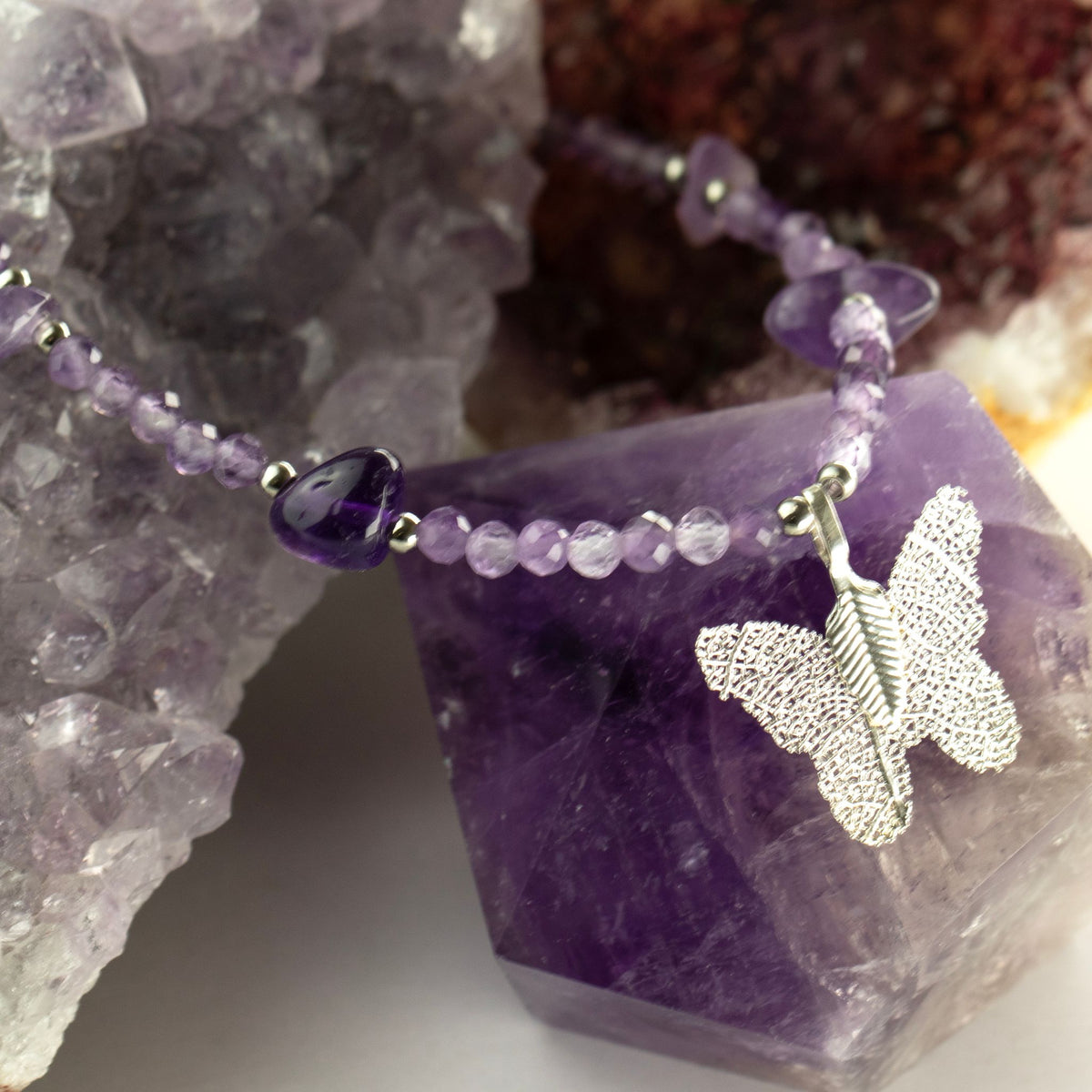 Close-up of amethyst necklace and butterfly pendant displayed on purple crystal