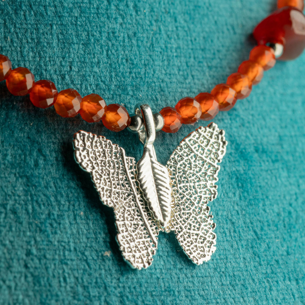 Close-up of silver-plated butterfly pendant with red Ruby gemstone beads