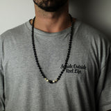 Person wearing a gray t-shirt with a black bead necklace.
