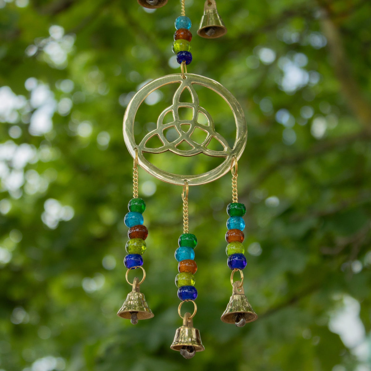 Celtic knot brass wind chimes hanging outdoors among green leaves