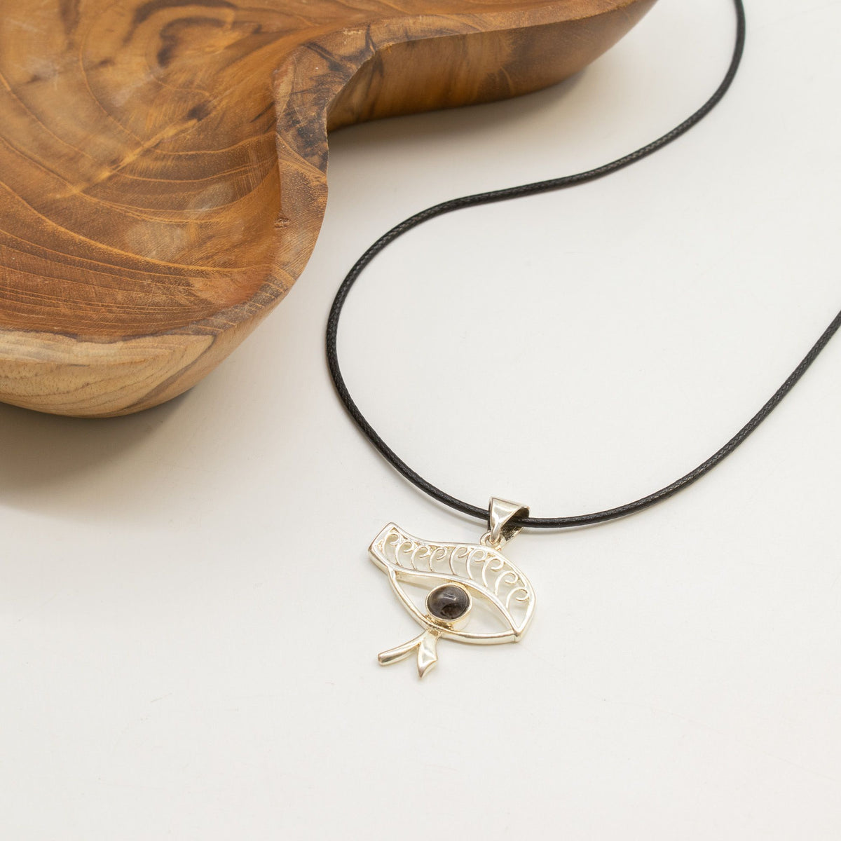 Cleopatra Eye necklace displayed beside wooden ornament