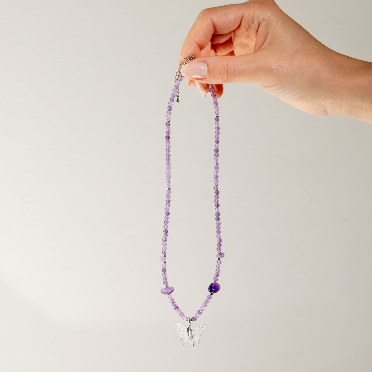 Amethyst gemstone necklace held up to show full length and butterfly pendant