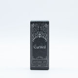Black packaging of 'Cursed' perfume oil with decorative design on a white background