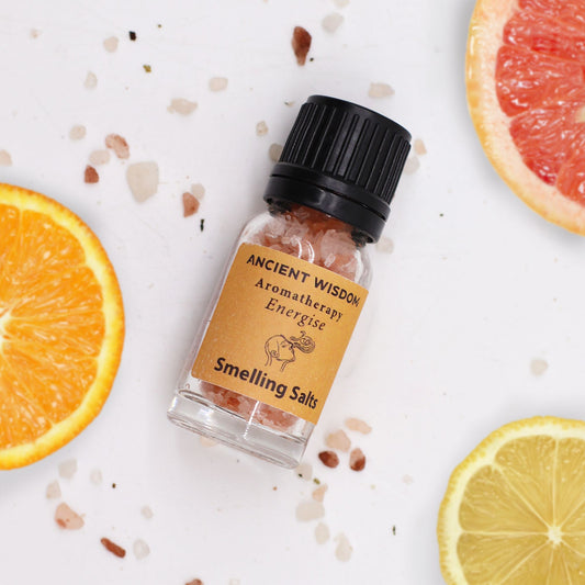 Bottle of 'Smelling Salts' from 'Ancient Wisdom Aromatherapy' with sliced oranges and lemons on a white background.