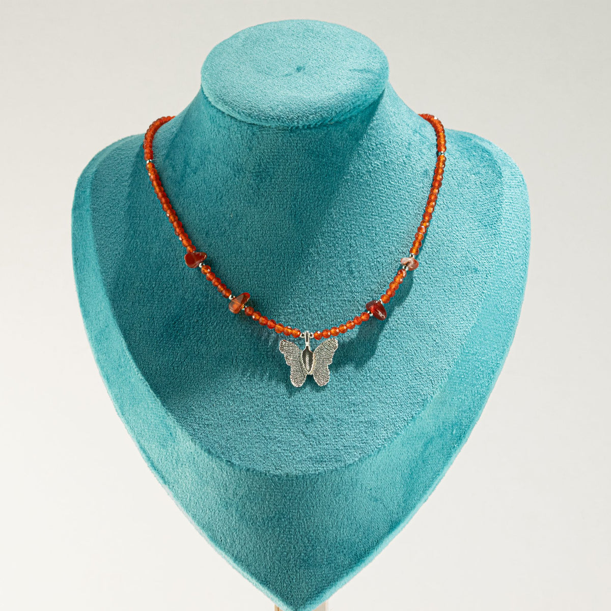 Ruby gemstone butterfly necklace displayed on turquoise jewellery bust