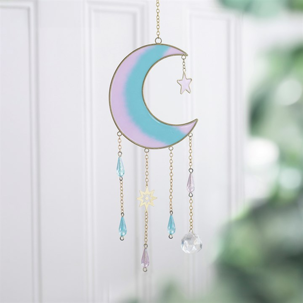 An iridescent pastel crescent moon and star suncatcher hanging in front of a white paneled door. The moon features a soft gradient of lavender, light blue, and mint green with gold-toned metal outlines, while hanging chains dangle light blue teardrop beads, a small gold star, and a clear faceted crystal ball.