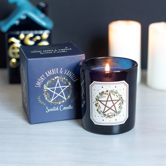 A lit dark blue glass scented candle with a white label featuring a pentagram and floral design.