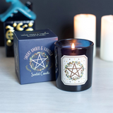 A lit dark blue glass scented candle with a white label featuring a pentagram and floral design.