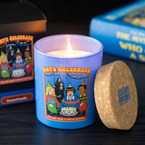 Lit candle in a blue container with a colorful label, surrounded by books and a cork coaster.