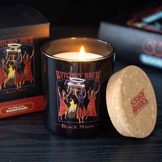 Candle labeled 'Witches' Brew Black Magic' with a cork lid and branded box in the background.